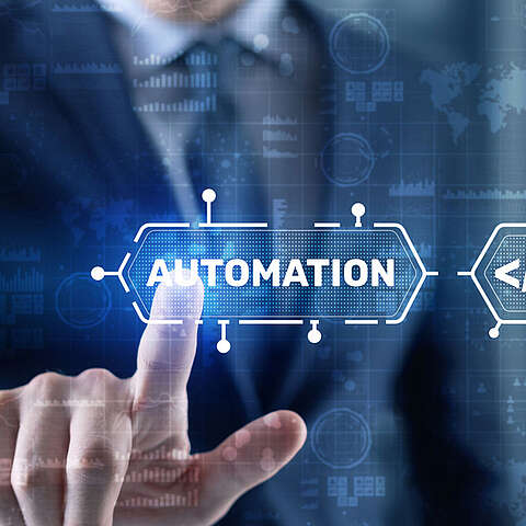 Eine Person in einem Anzug berührt einen virtuellen Bildschirm, auf dem das Wort "AUTOMATION" hervorgehoben ist, umgeben von digitalen Schnittstellengrafiken und einer verschwommenen Weltkarte im Hintergrund.