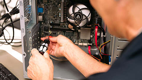 Eine Person arbeitet mit einem Schraubenzieher im Inneren eines geöffneten Desktop-Computergehäuses und justiert Komponenten in der Nähe der Hauptplatine und des Lüfters.
