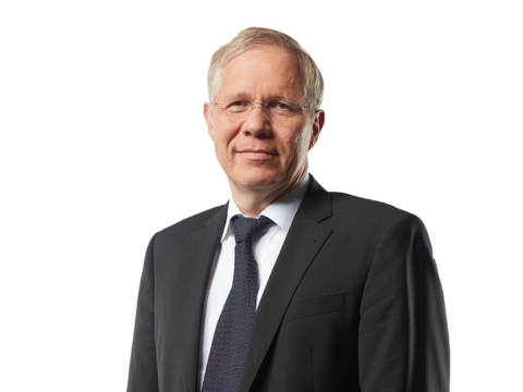 Mann mit schwarzem Sakko, weißem Hemd und blauer Krawatte lächelt in die Kamera