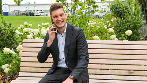 Junger Mann im Anzug sitzt auf einer Parkbank im grünen telefoniert