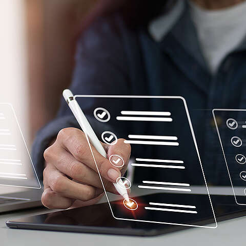 Eine Person verwendet einen Stift, um Punkte auf einer digitalen Checkliste abzuhaken, die auf einem Tablet angezeigt wird, während andere digitale Listen im Hintergrund sichtbar sind.