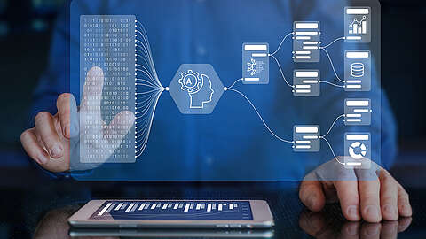 Eine Person interagiert mit einer virtuellen Schnittstelle, die KI- und Datenflussdiagramme, Binärcode, Diagramme und Datenknoten zeigt, während ein Tablet mit Balkendiagrammen auf einer reflektierenden Oberfläche liegt.