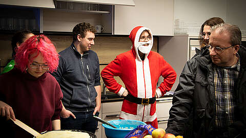 Mehrere Menschen in einer Küche, von denen eine Person als Weihnachtsmann verkleidet ist