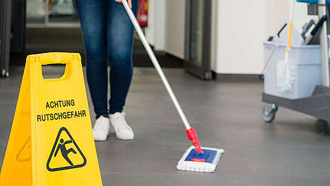Facility Management beim Q-FOX® Person, die den Boden wäscht und ein Warnschild