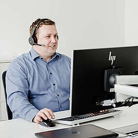 Consulting Mitarbeiter sitzt am PC und telefoniert über ein Headset