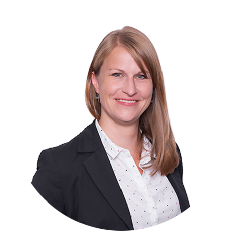 Eine Frau mit glattem hellbraunem Haar, die einen schwarzen Blazer über einem weißen Button-up-Hemd mit kleinen schwarzen Punkten trägt, steht lächelnd vor einem schlichten weißen Hintergrund.