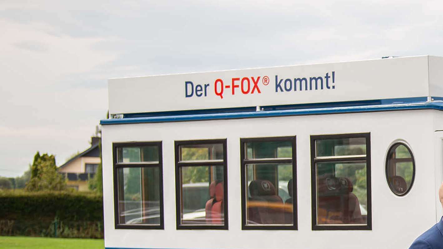 Drei Menschen stehen vor einem Bus mit dem Q-FOX® Logo