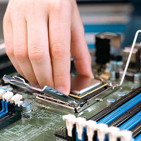 Nahaufnahme eines offenen Computer-Motherboards mit leerem CPU-Sockel. Die metallisch-grünen Schaltkreise sowie Pins und Anschlüsse sind sichtbar und ermöglichen einen detaillierten Blick in die interne Hardware eines Computers.