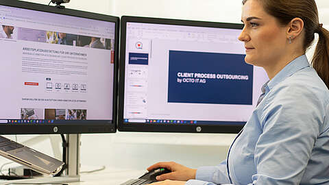 Eine Frau in einem blauen Hemd arbeitet an einem Schreibtisch mit zwei Bildschirmen; auf dem einen ist eine Website zu sehen, auf dem anderen eine Folie mit dem Titel „CLIENT PROCESS OUTSOURCING by OCTO IT AG“.