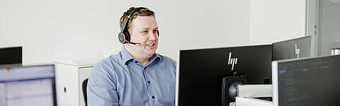 Consulting Mitarbeiter sitzt am PC und telefoniert über ein Headset