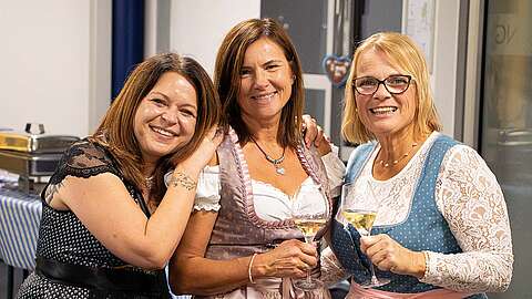 3 lachende Mitarbeiterinnen im Dirndl und mit einem Sekt in der Hand