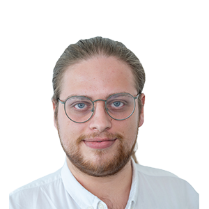 Ein Mann mit heller Haut, Brille, hellbraunem, nach hinten gebundenem Haar und Bart, der ein weißes Hemd mit Kragen trägt, lächelt leicht vor einem schlichten weißen Hintergrund.