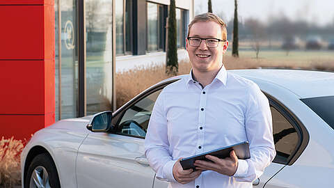 Mitarbeiter im weißen Hemd steht vor einem Auto und hat ein Tablet in der Hand