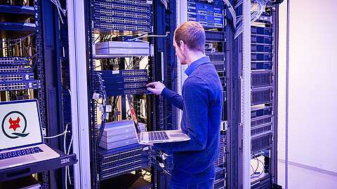 Mitarbeiter steht vor einem Serverschrank und hat einen Laptop in der Hand