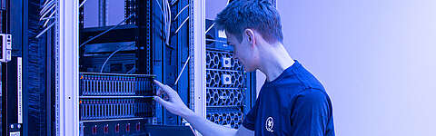 Q-FOX® Mitarbeiter drückt auf einen Kopf an einem Serverschrank und hat einen Laptop in der Hand